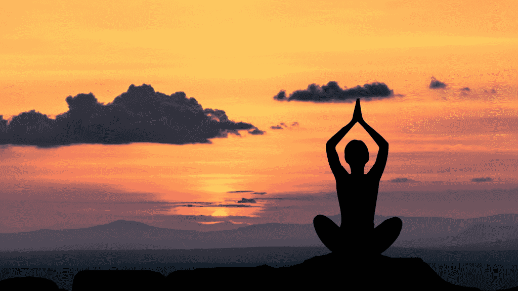 Uma pessoa meditando em meio a um pôr do sol.