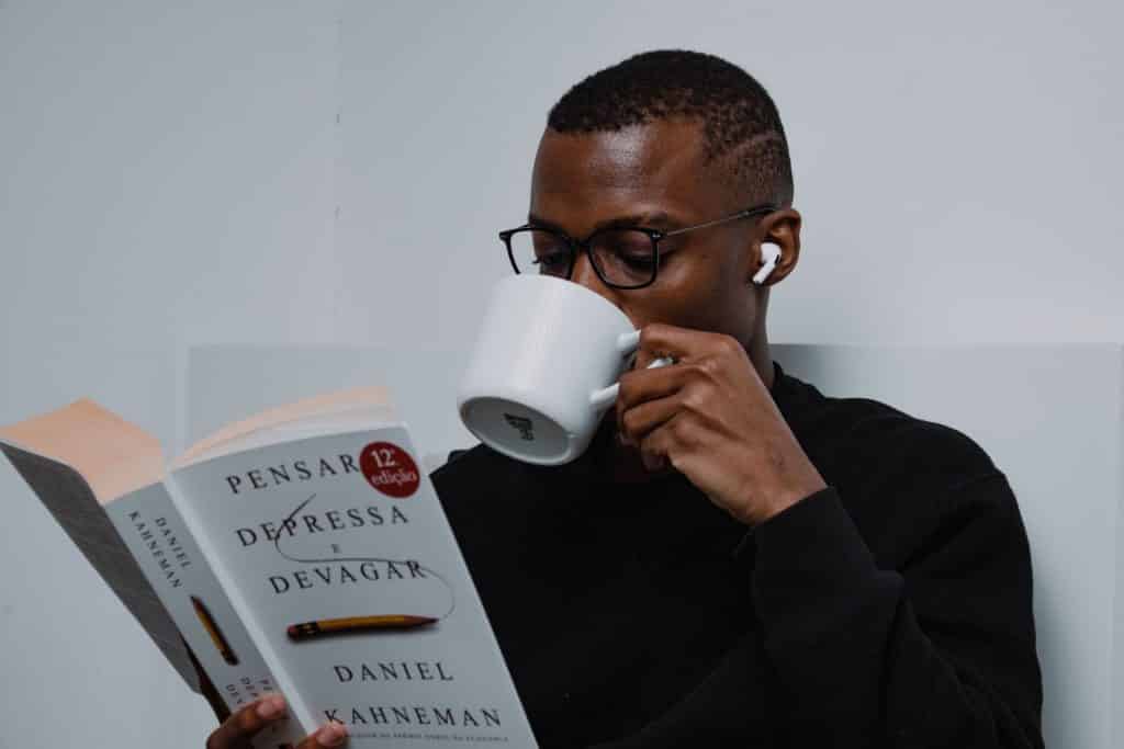 Homem lendo um livro e tomando uma xícara de café.