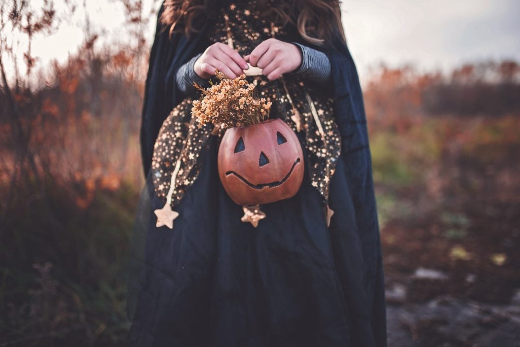 Menina fantasiada segurando uma cestinha de pedir doces em dia das bruxas.