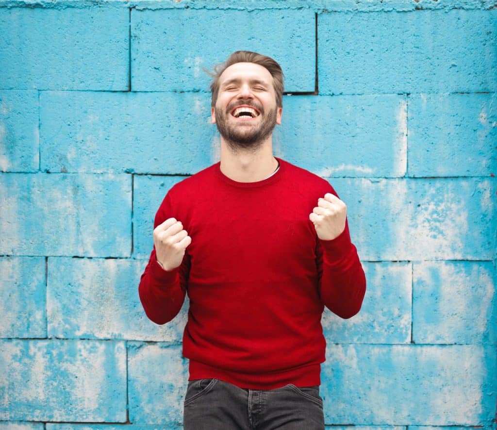 Homem sorrindo e em pose de comemoração.