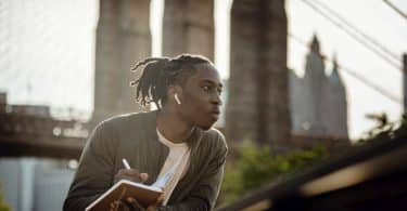 Homem negro segurando caderno e olhando pra o lado.