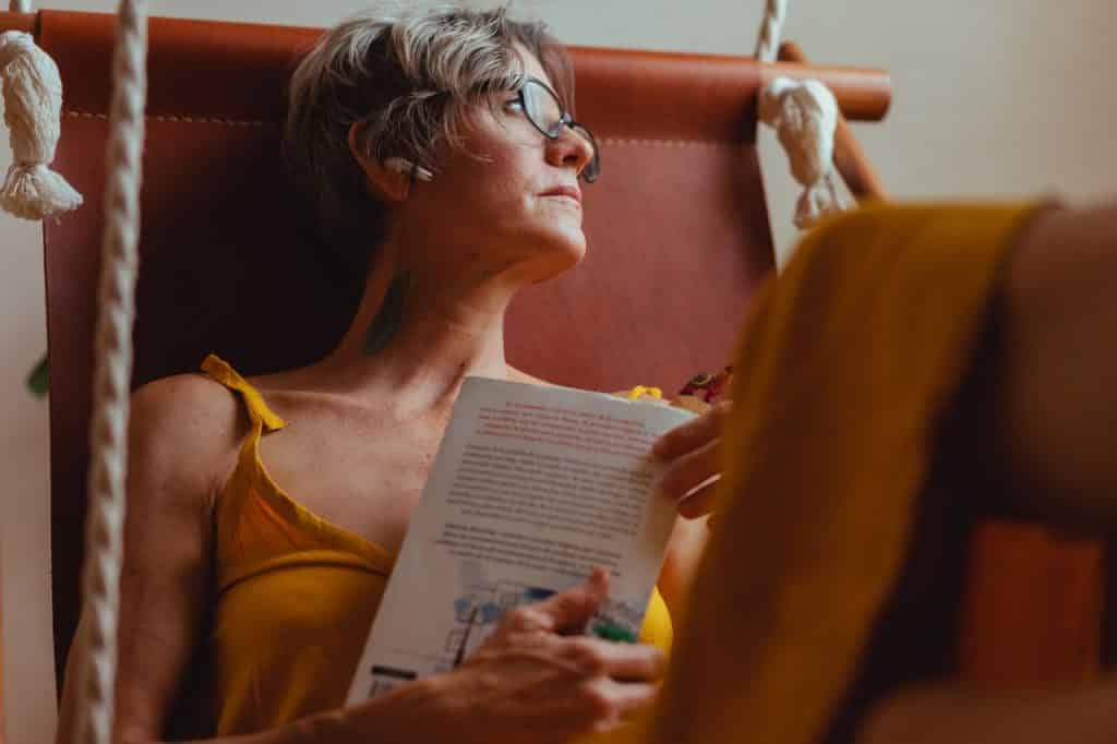 Mulher segurando um livro e olhando para o lado com semblante pensativo.