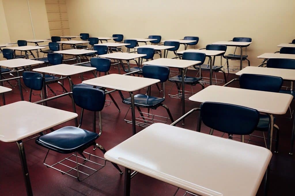 Sala de escola cheia de mesas e cadeiras vazias.