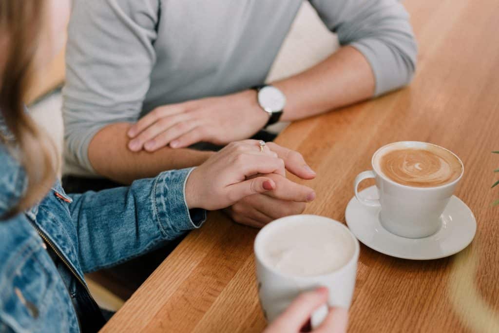 Casal tomando café e segurando a mão um do outro.