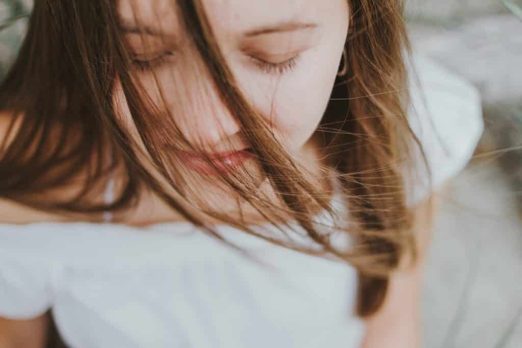 Jovem branca de olhos fechados e cabelo no rosto.