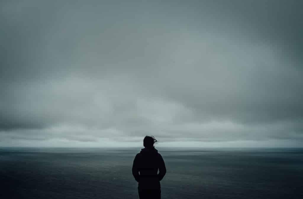 Homem em frente ao mar, o céu está cinza.