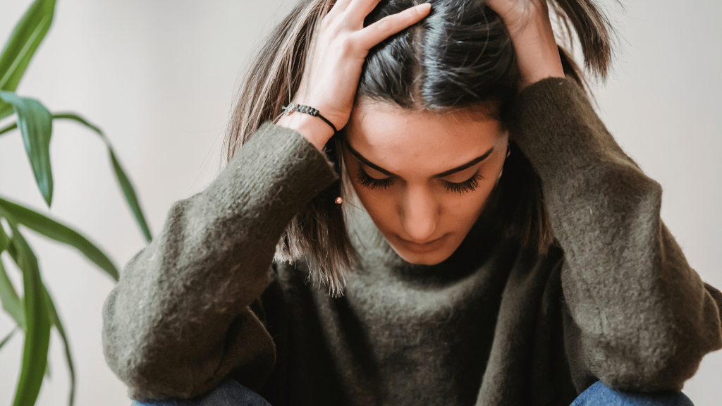 Mulher de olhos fechados e cabeça abaixada com as mãos no cabelo