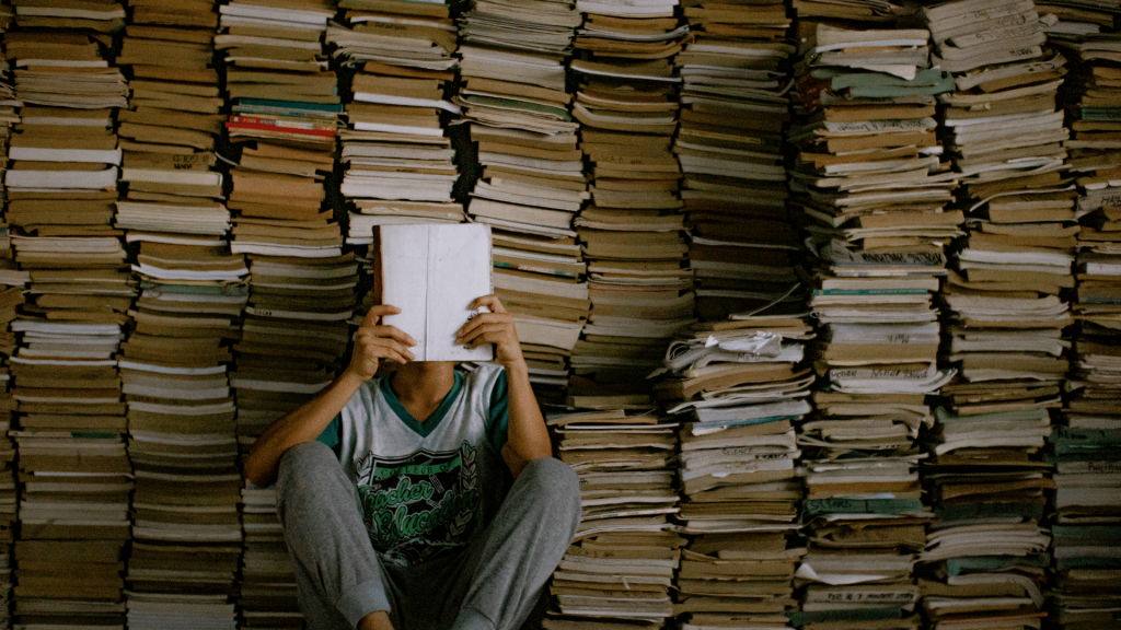 Pessoa segurando um livro na altura do seu rosto conforme o lê