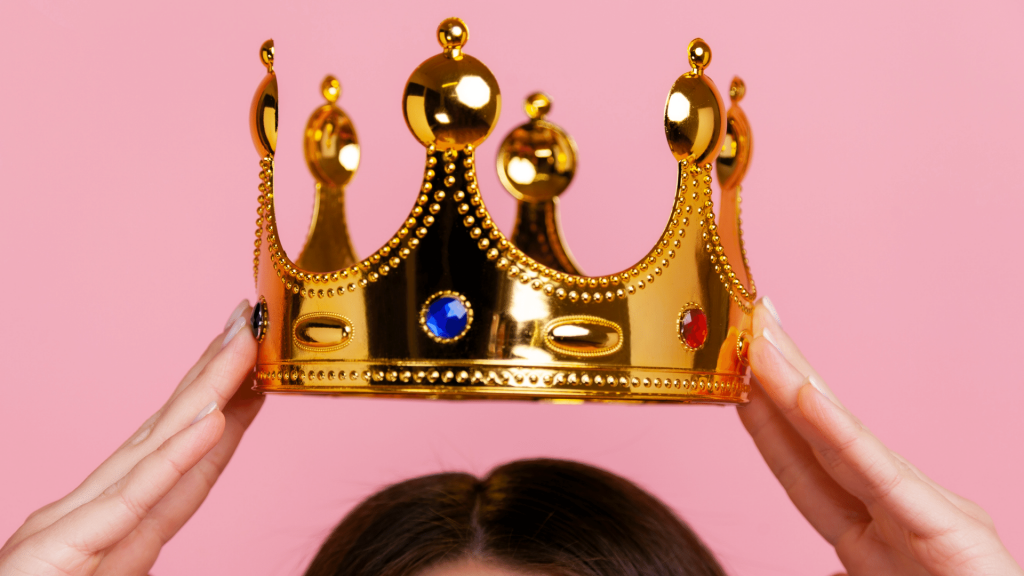 Mulher segurando uma coroa dourada de plástico com as duas mãos por cima da sua cabeça
