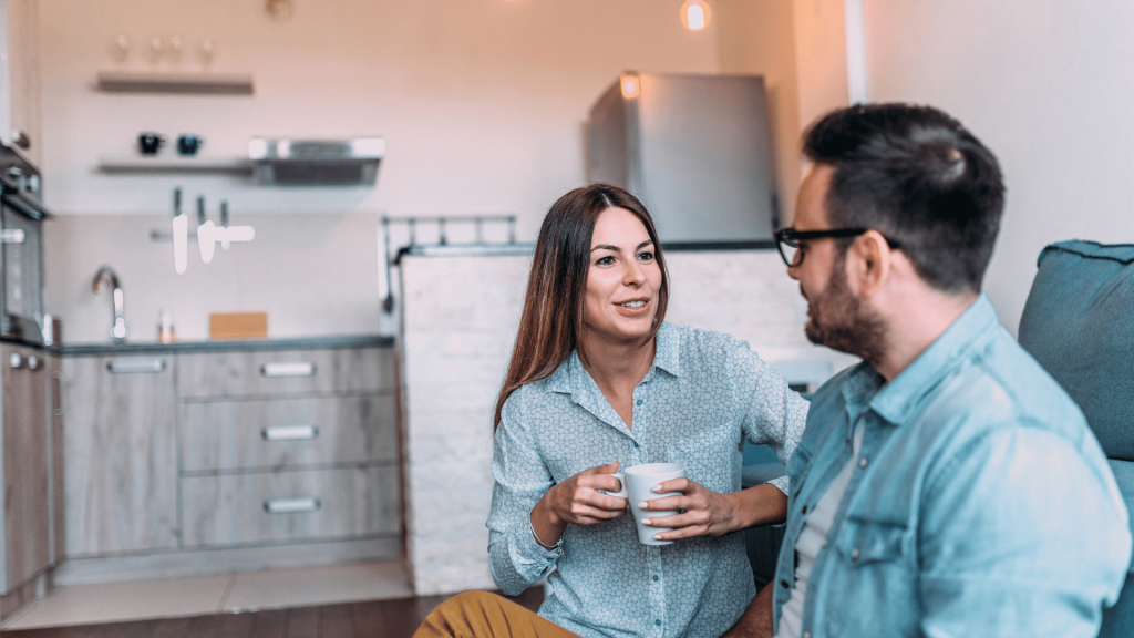 Casal composto por um homem e uma mulher conversando sentados no sofá