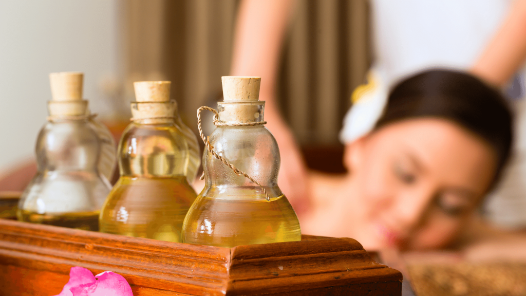 Potes de vidro contendo óleos de massagem enquanto uma mulher recebe uma massagem