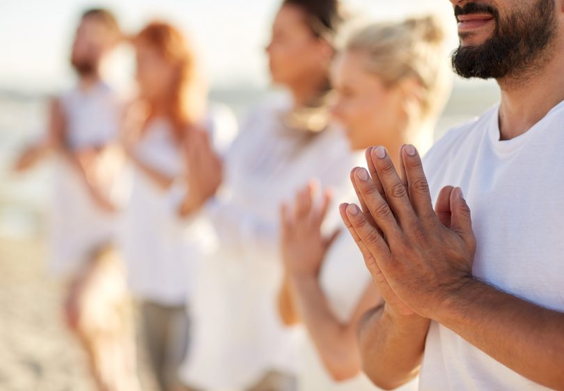 Grupo de pessoas fazendo namastê na praia