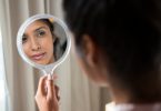 Mulher segurando espelho de mão e olhando para seu próprio reflexo
