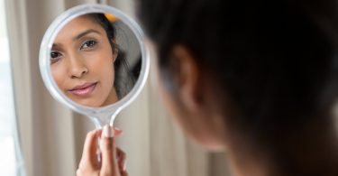 Mulher segurando espelho de mão e olhando para seu próprio reflexo