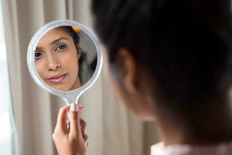 Mulher segurando espelho de mão e olhando para seu próprio reflexo