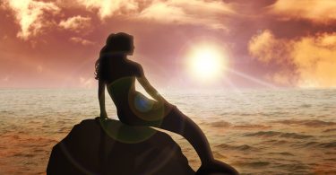 Silhueta de uma sereia sentada em uma pedra ao pôr-do-sol