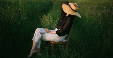 Uma mulher sentada numa cadeira situada ao meio de um gramado.