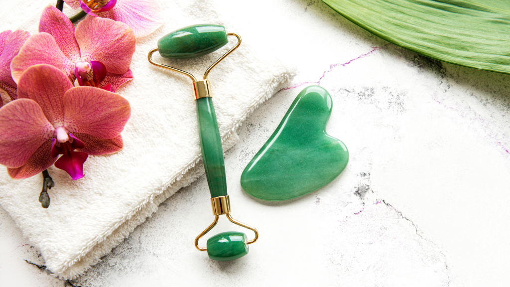 Rolo de jade para o rosto em uma mesa com uma pedra de jade ao lado, toalha e orquídeas