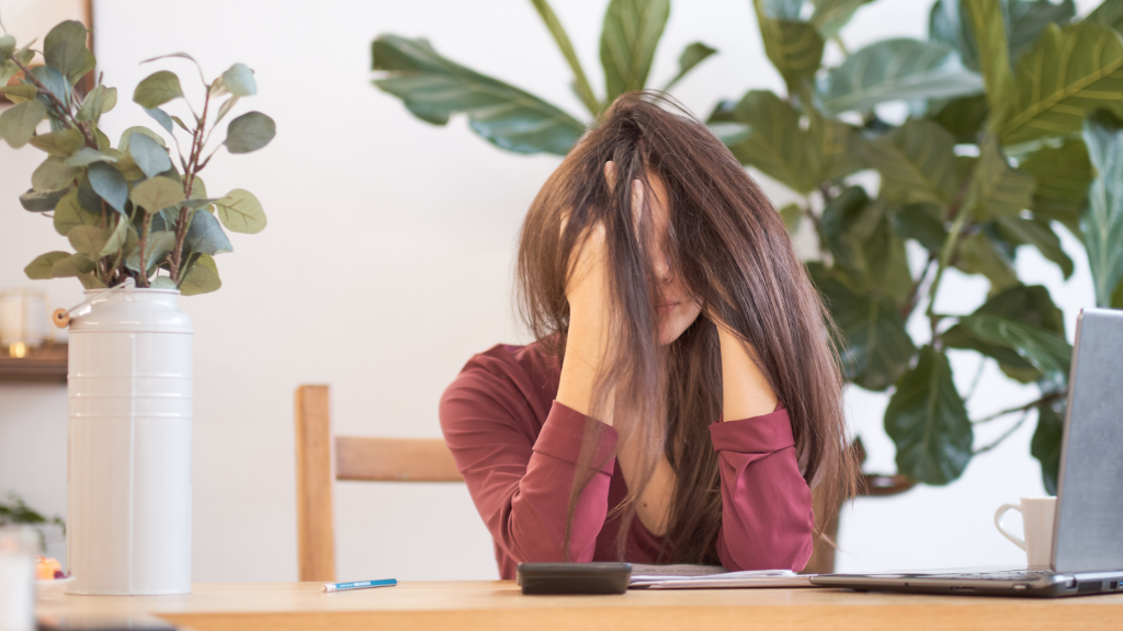 Mulher estressada em frente ao notebook. Seus cabelos estão bagunçados cobrindo o rosto