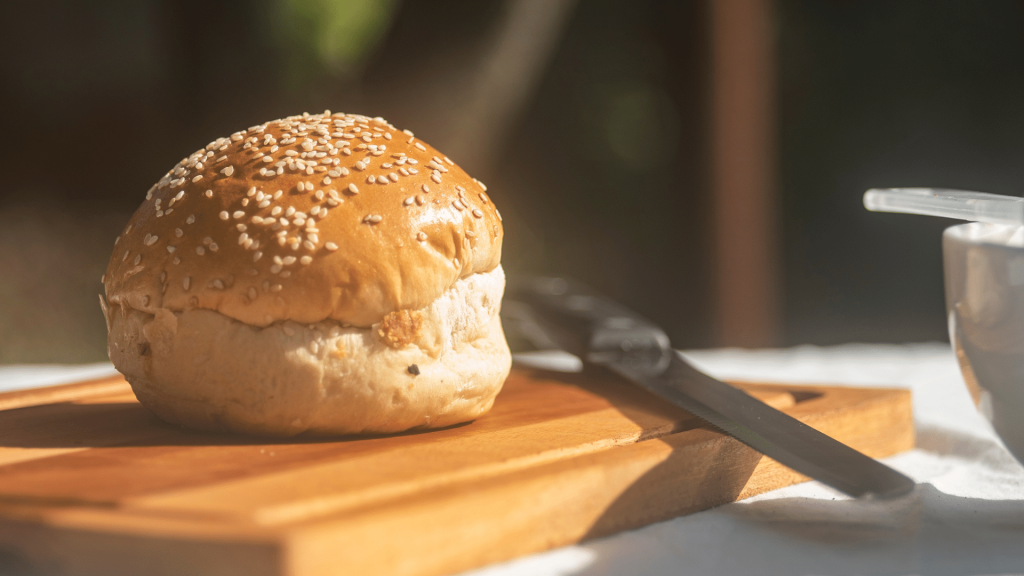 Pão de hambúrguer assado em cima de uma tábua de madeira ao lado de uma faca