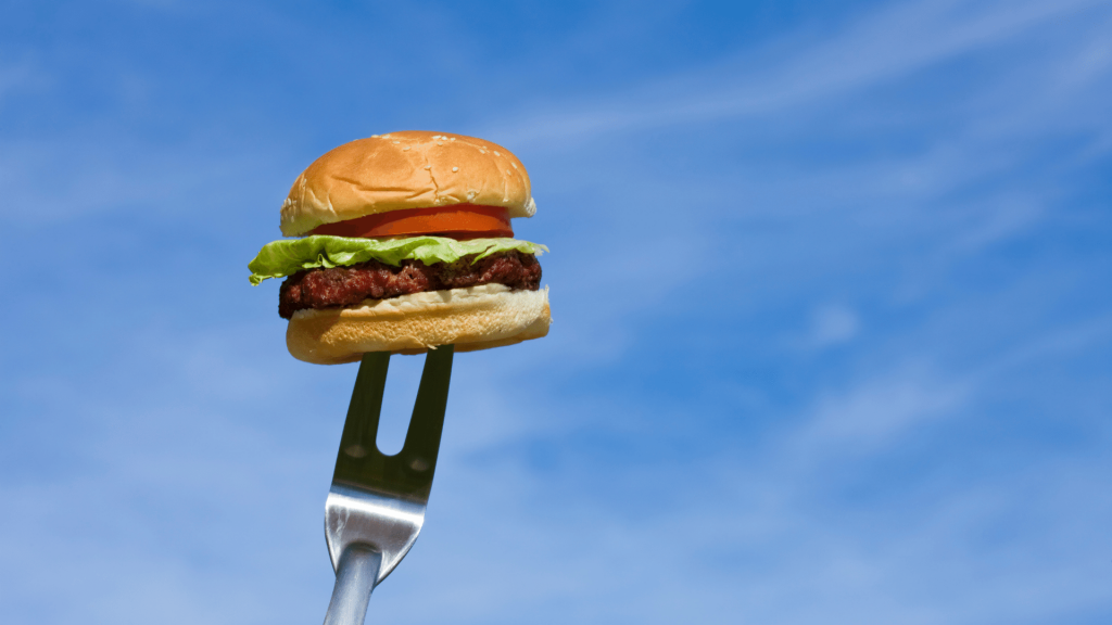 Pequeno lanche recheado de hambúrguer, alface e tomate espetado por um garfo