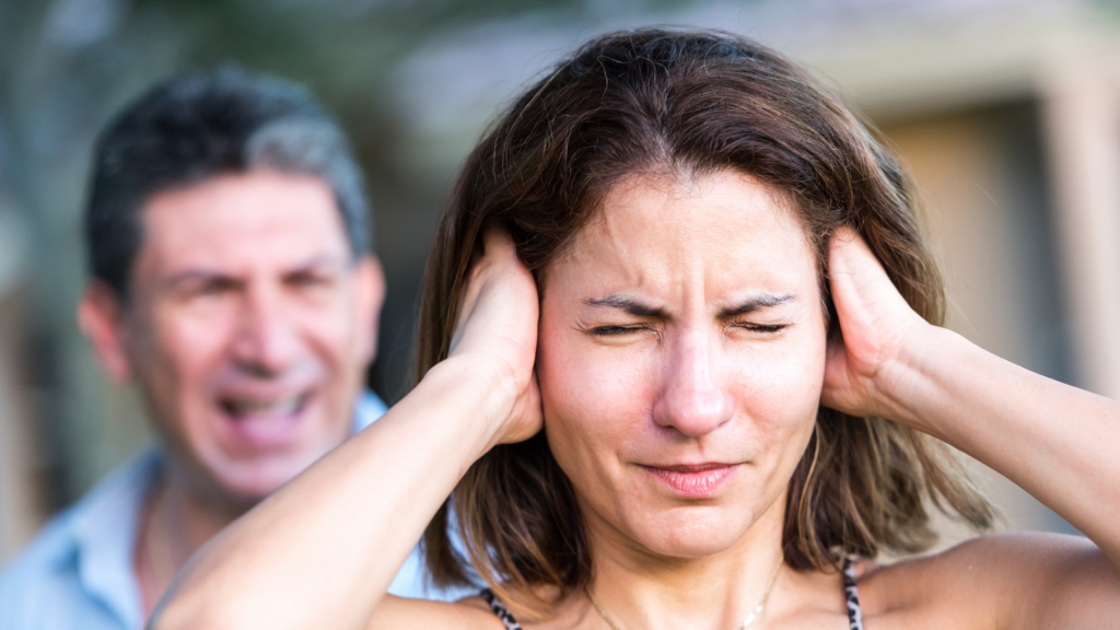 Um homem gritando com uma mulher. Esta, por sua vez, tapa seus ouvidos com as mãos.