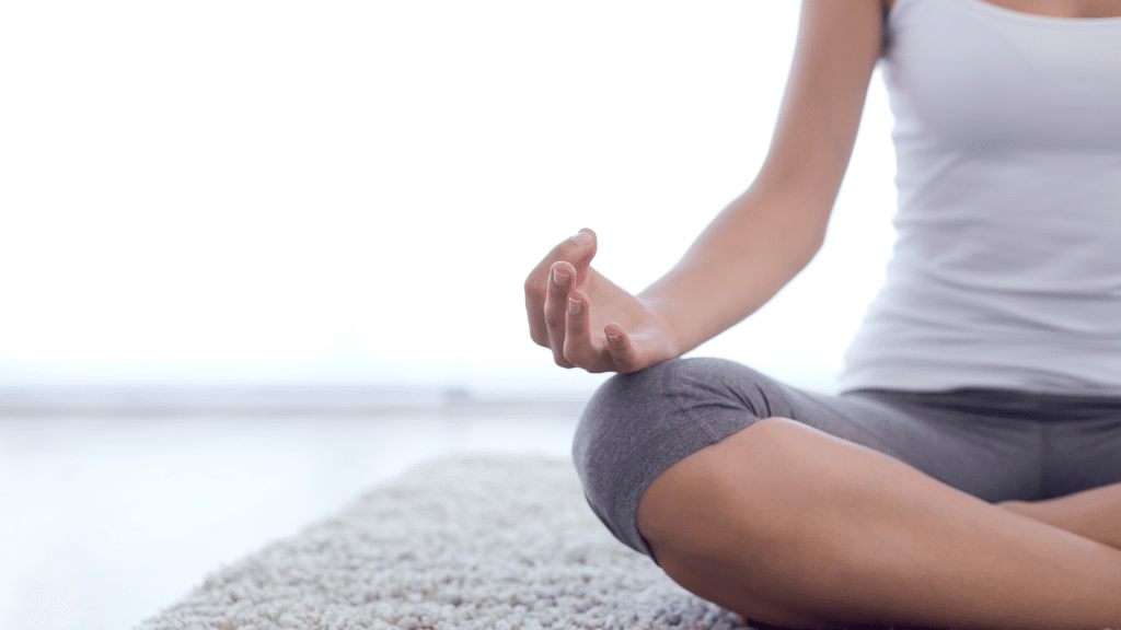 Sentada num tapete, uma pessoa meditando.