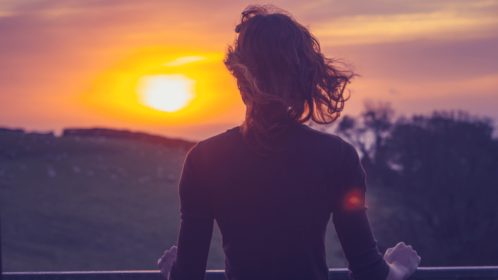 Uma pessoa contemplando um forte nascer ou raiar do sol.