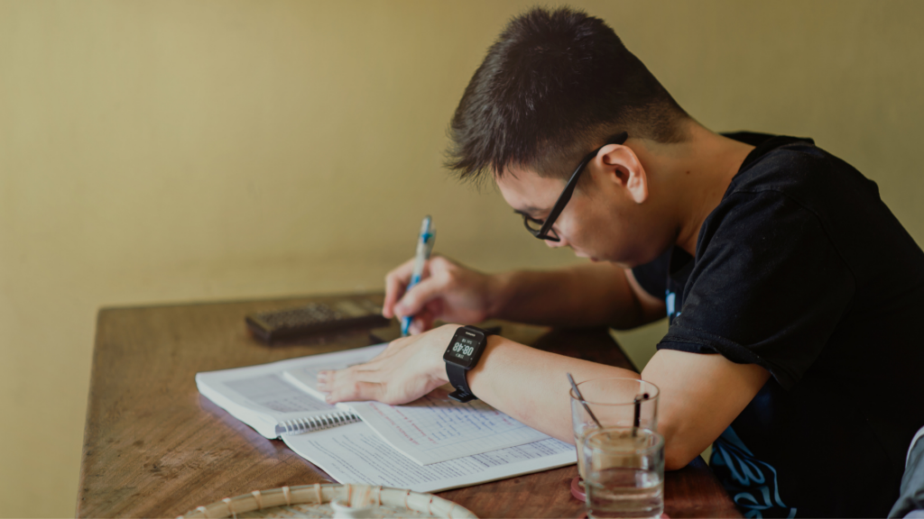 Sentado à mesa, um homem realizando anotações em um caderno.