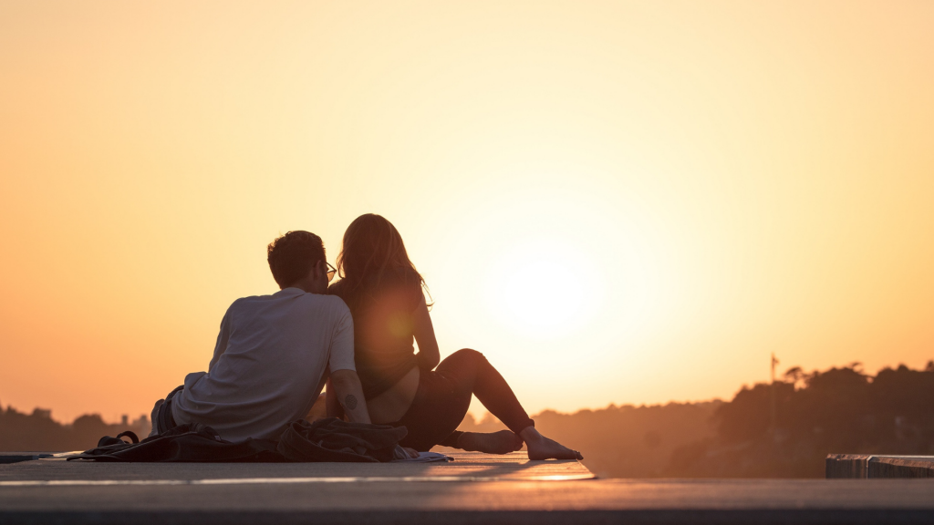Um casal heterossexual à beira de um pôr do sol.