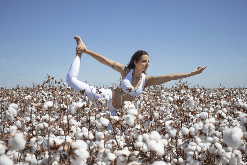 Mulher em um campo de algodão fazendo Yoga.