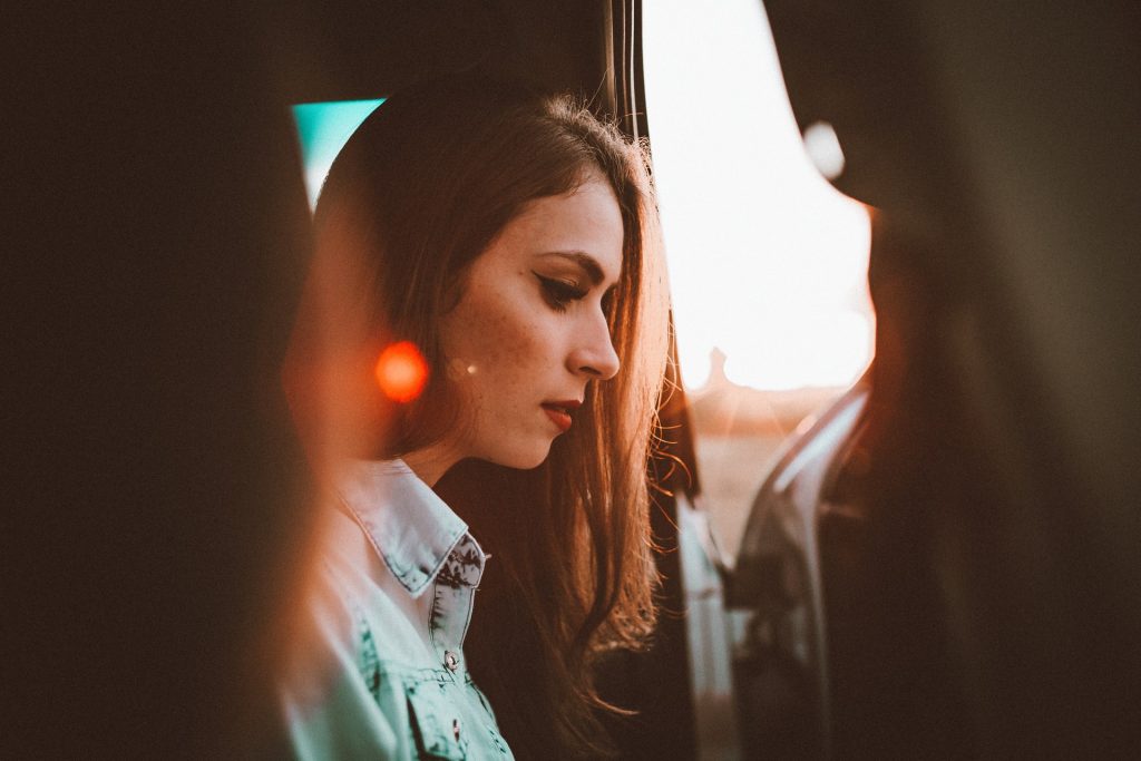 Mulher branca num carro de cabeça baixa.