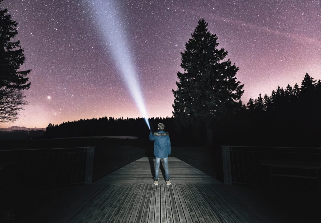 Homem apontando uma lanterna para o céu a noite.