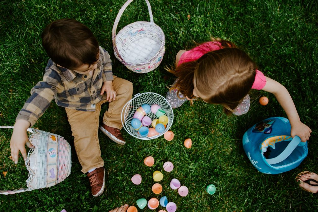 Crianças na grama brincando com ovos coloridos.