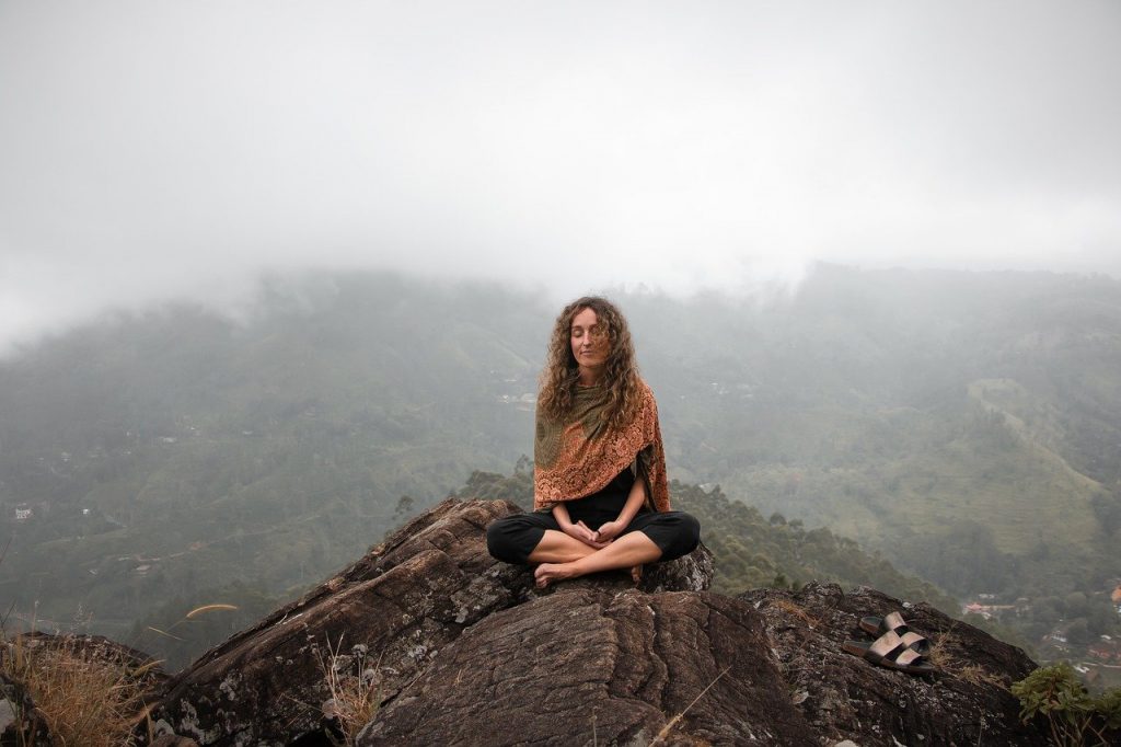 Mulher meditando sobre rocha no alto de uma montanha