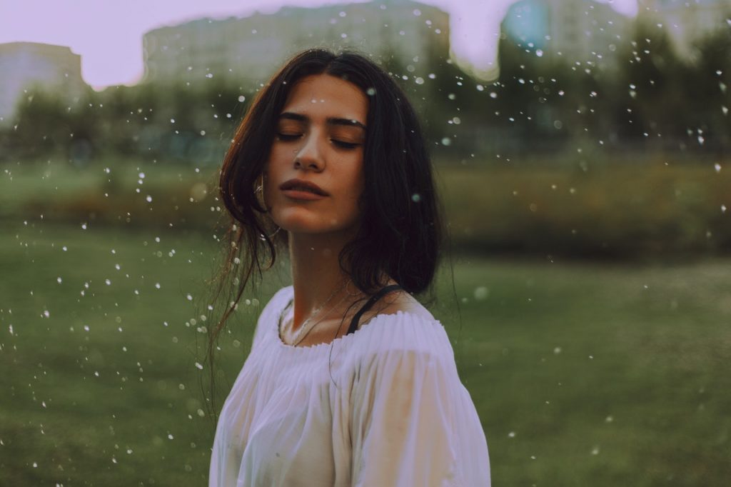 Mulher branca de olhos fechados na chuva.