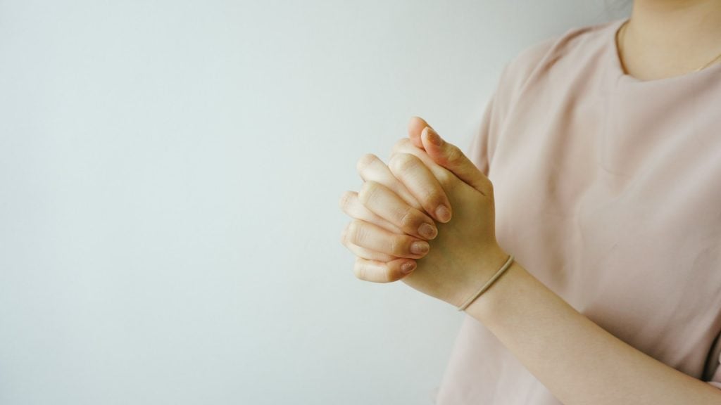 Mãos femininas juntas em forma de oração.