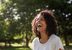 Mulher negra sorrindo. Ela está em um parque.