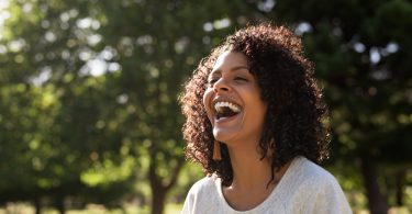 Mulher negra sorrindo. Ela está em um parque.