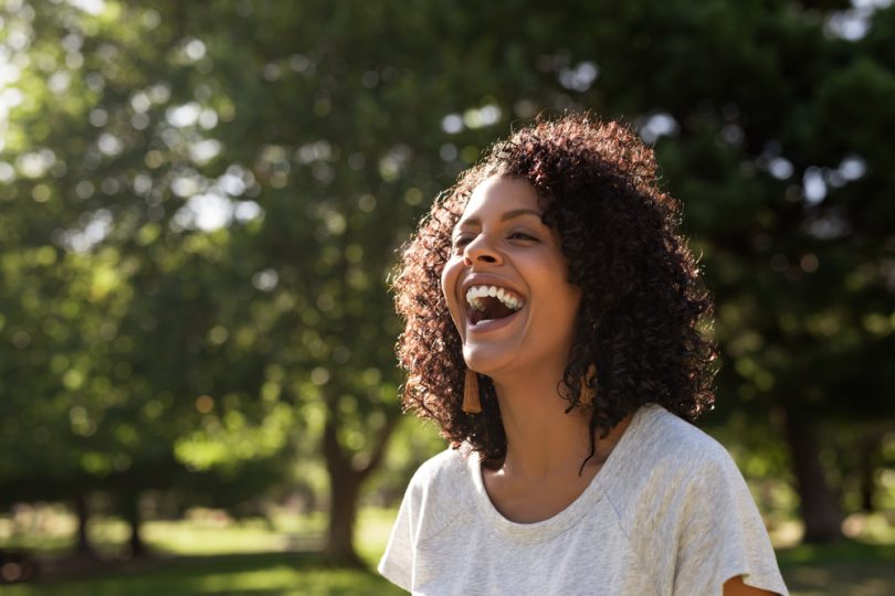 Mulher negra sorrindo. Ela está em um parque.