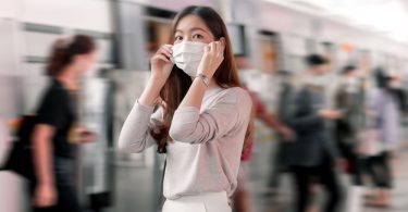 Mulher asiática em uma estação de metrô com máscara.