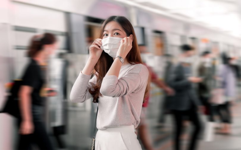 Mulher asiática em uma estação de metrô com máscara.