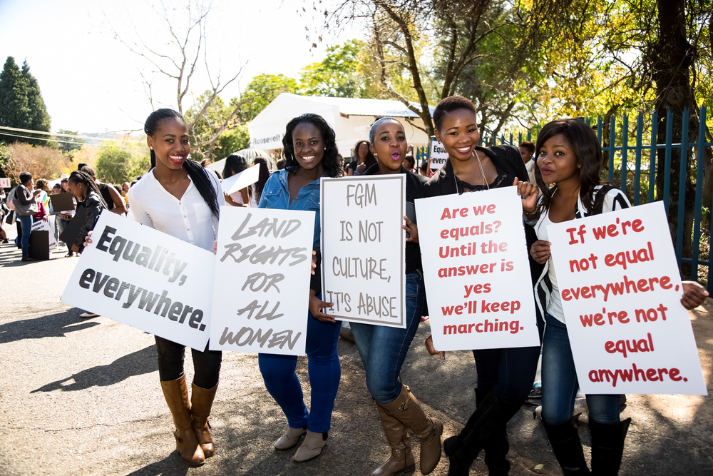 Cinco mulheres negras com cartazes com frases feministas protestando na rua