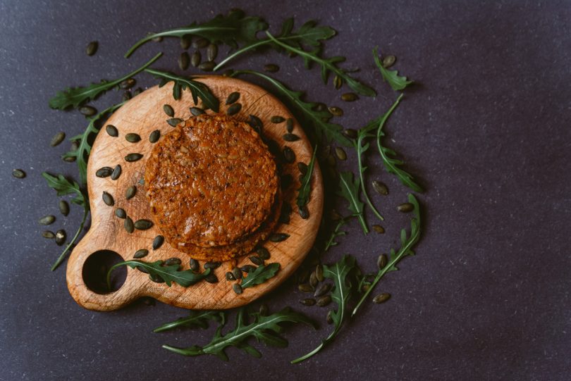 Hambúrgueres veganos sobre uma tábua de madeira envoltos com temperos