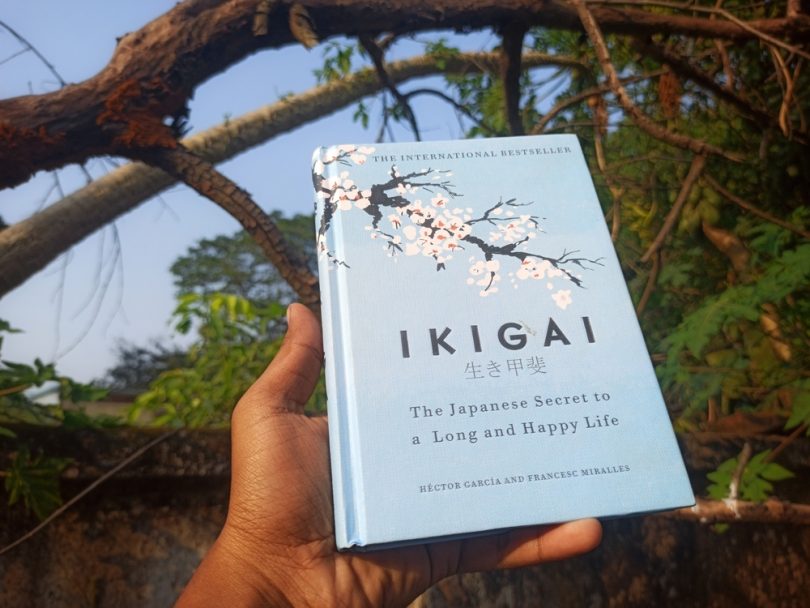 Mão humana segurando um livro cujo o escrito "Ikigai" está na capa.