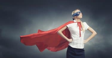 Mulher em uma pose de poder de super-herói usando uma capa e com uma máscara nos olhos