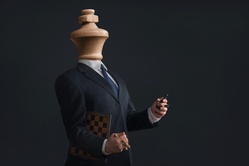 Homem branco com peça de xadrez no lugar da cabeça.