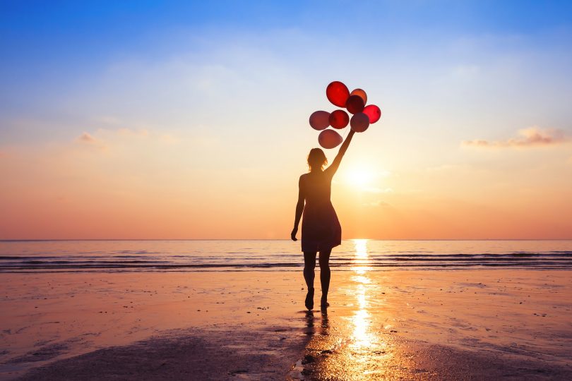 Uma mulher de pé em frente ao mar. Ela segura balões de ar.