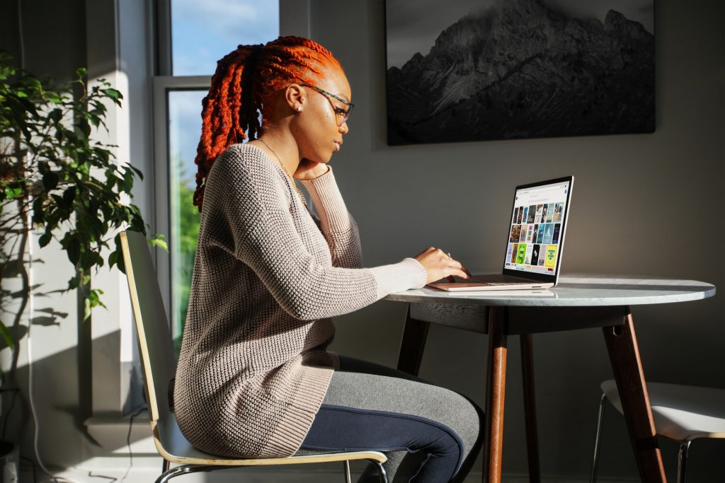 Mulher sentada em uma mesa de home office mexendo em um notebook.