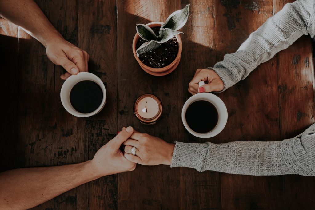 Casal com as mãos dadas enquanto tomam café.